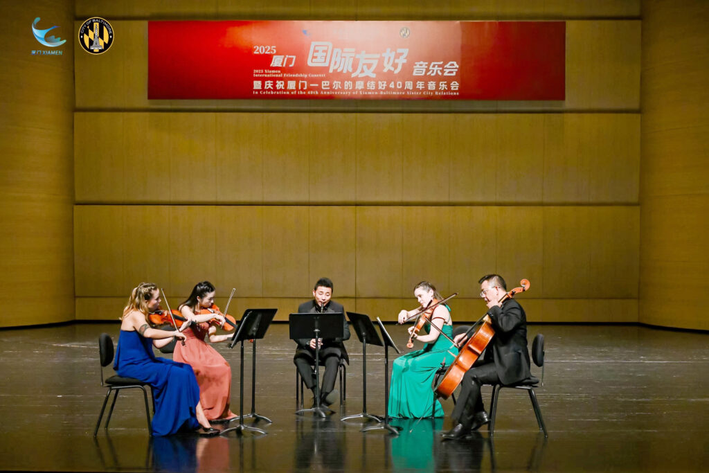 5 musicians from Baltimore Symphony Orchestra performing music on a stage in Xiamen on October 28, 2025. Above the stage is a banner marking the 40th anniversary of the Baltimore-Xiamen Sister City relationship. Photo by Xiamen FAO.