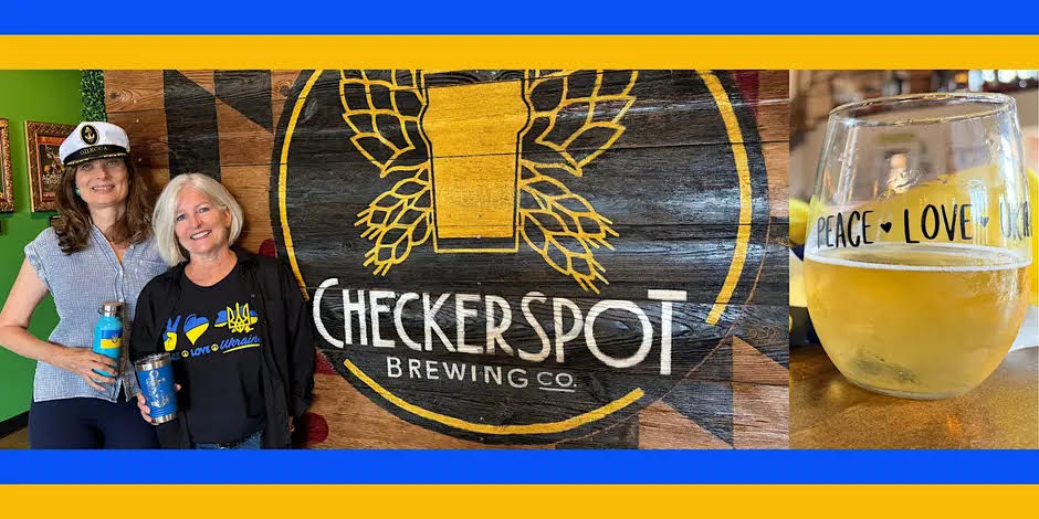Two female brewers standing in front of brewing companies logo with a picture of beer beside them.