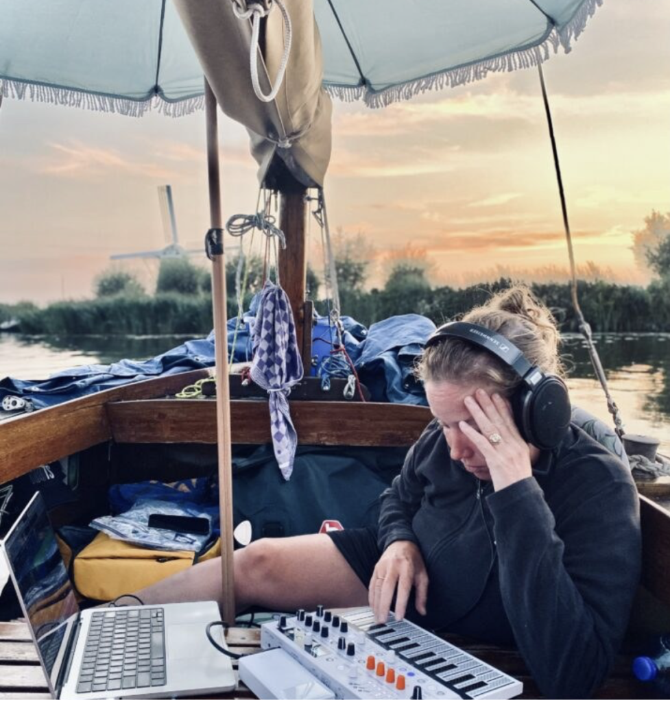 Vivienne Aerts sitting in a boat with headphones on working on a project with her computer and portable piano. 