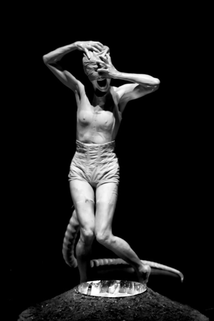 Black and white photo of a person grabbing their face that is wrapped in fabric while screaming. 